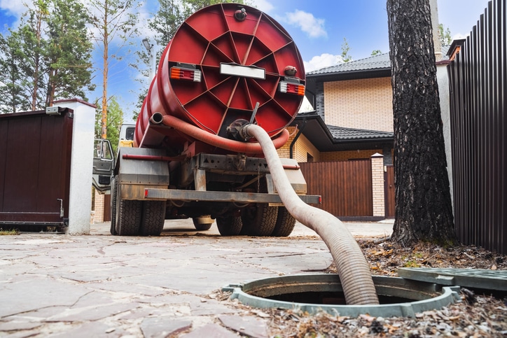 sewage truck with a large red tank using a hose to service an underground septic system