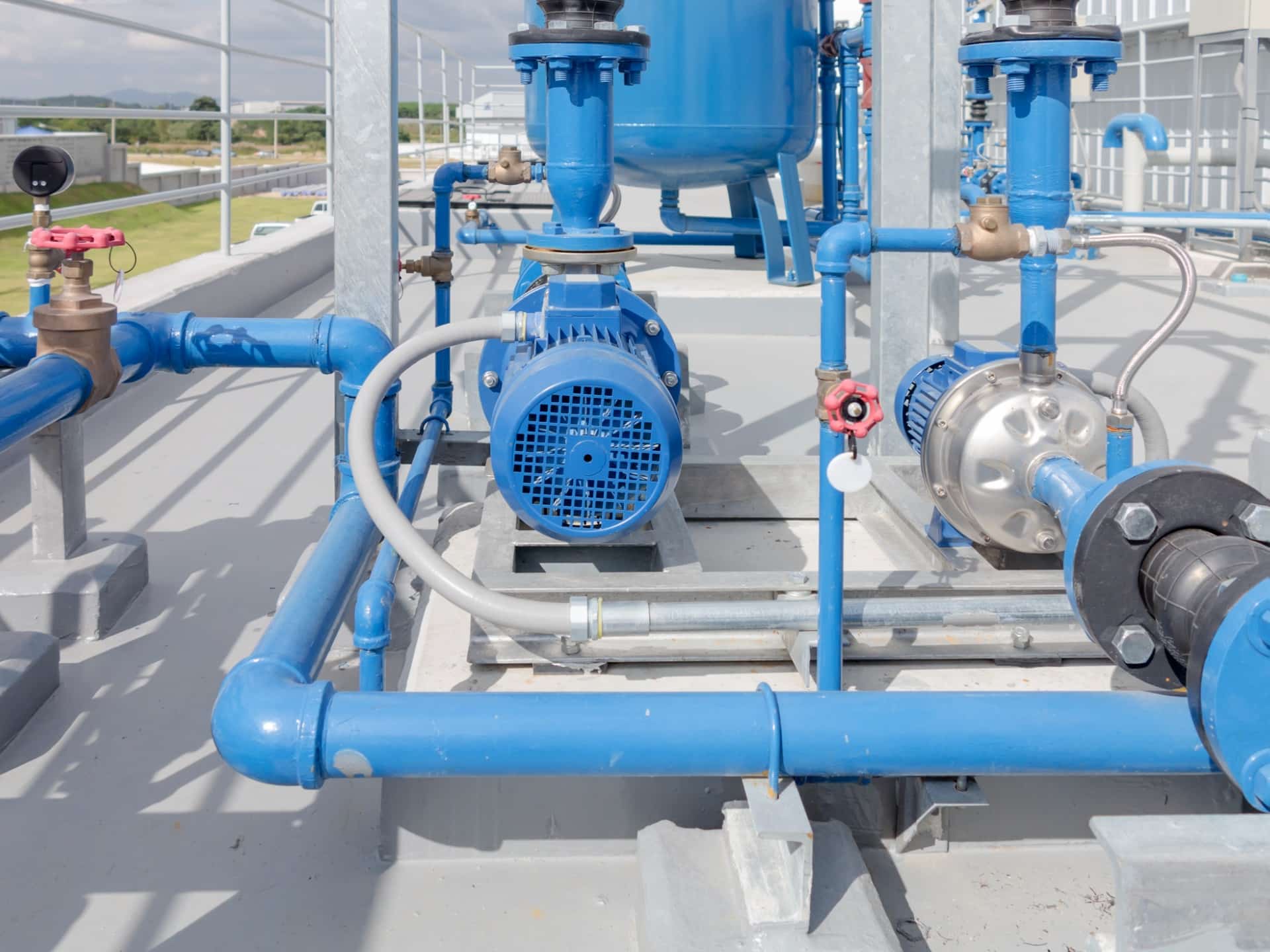 Blue industrial pumps and pipes on a rooftop, shining under sunlight. The setup includes valves and gauges, suggesting a modern, functional facility.