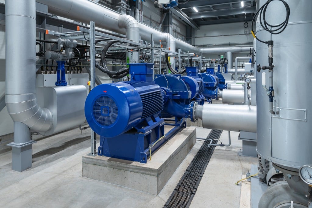 Industrial facility with large blue industrial pumps and silver pipes. The setting is clean and well-organized, suggesting efficiency and modernity.